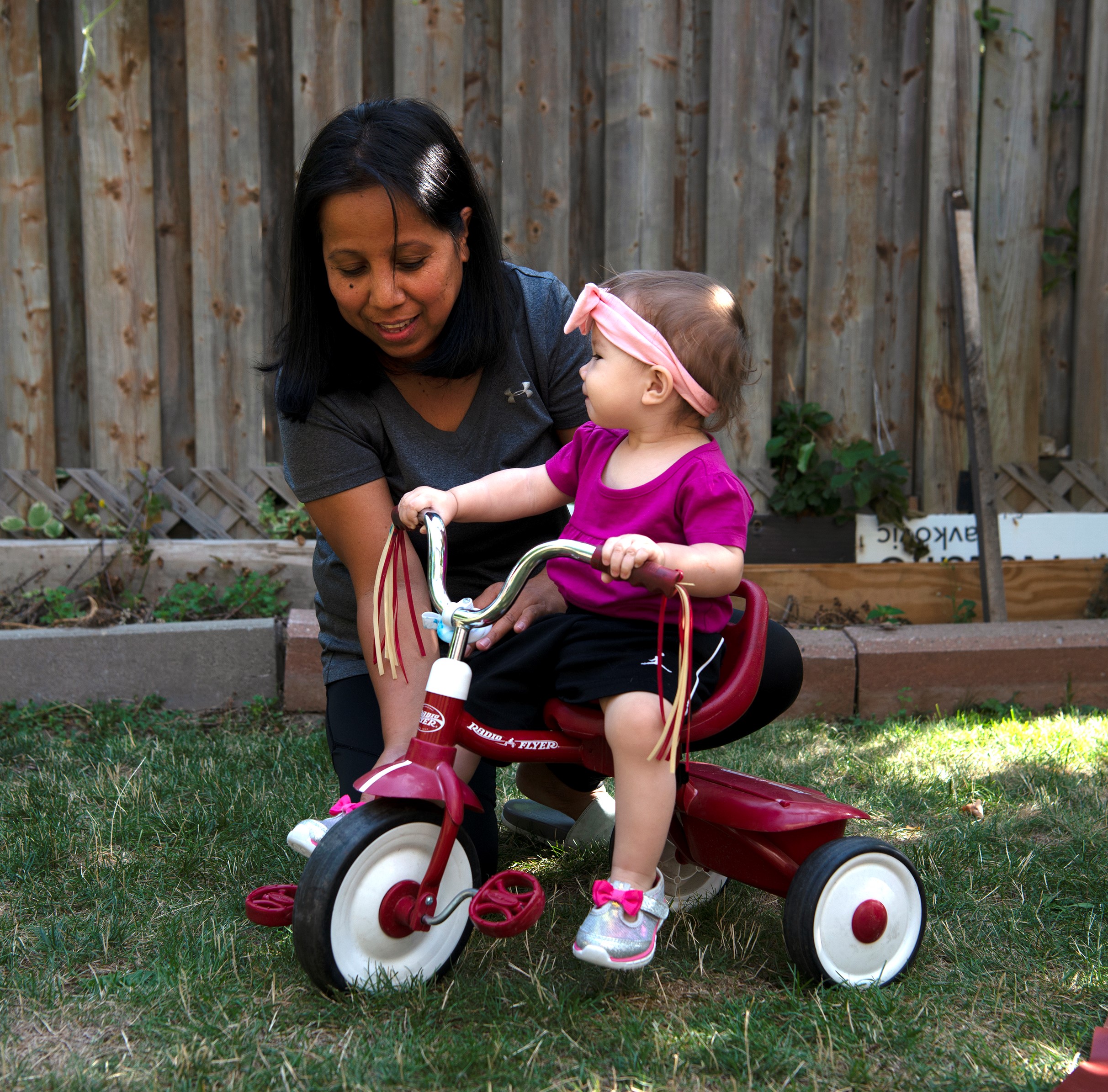 licensed home child care provider helping a toddler ride a tricycle