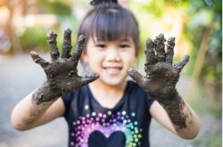 happy child holding up hands covered in mud on international mud day